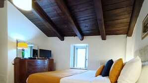 A bedroom with a wooden ceiling, a bed with white and orange bedding, a dresser, a television, and a window. - Monastero del Palazzo Casa Vacanze, apartment with panoramic terrace (Spoleto)