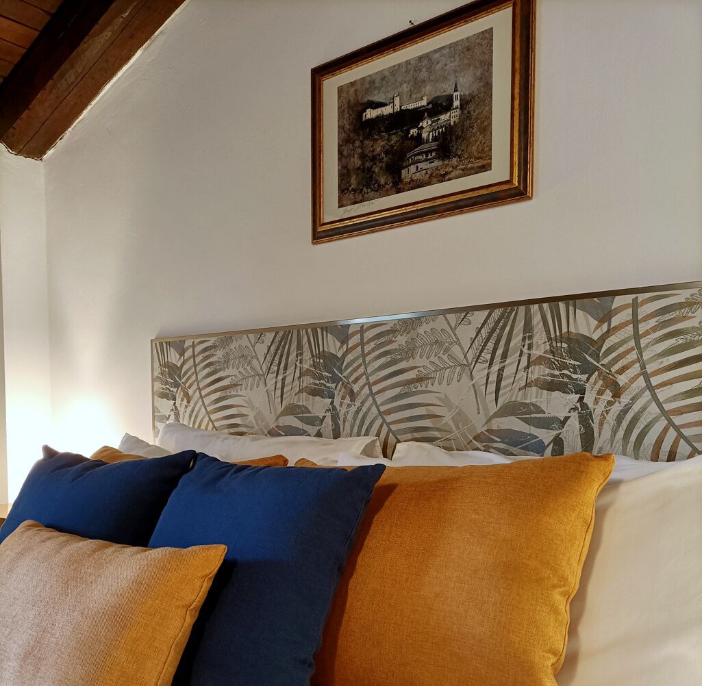A bedroom with a bed, pillows, a framed picture on the wall, and a ceiling with wooden beams.