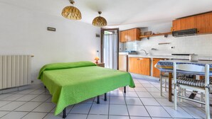 Una habitación pequeña con cama, una mesa y sillas, una zona de cocina y un radiador.