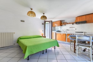 Una stanza compatta con un letto, un tavolo con sedie, angolo cottura e termosifone.