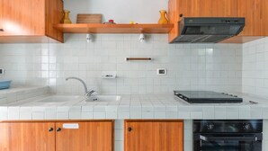 Una cocina con azulejos blancos, armarios de madera, un lavamanos de acero inoxidable y un horno empotrado.