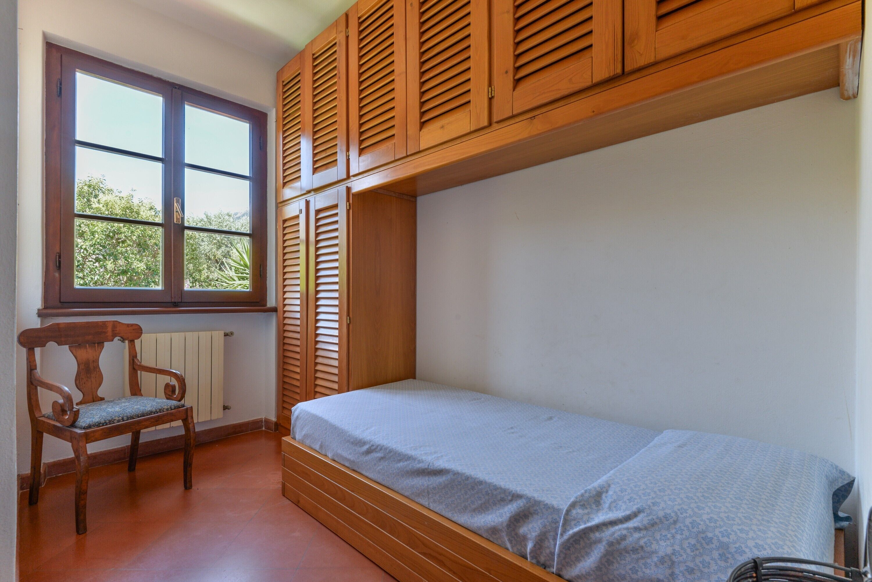 A room with a single bed, a wooden chair, a window, and wooden shutters.