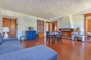 Un vaste espace de vie comprenant un canapé, une table à manger avec des chaises, une cheminée et des portes en bois.