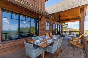 A wooden deck with a dining table set for six, surrounded by wicker chairs. - Bella Vista at Eagles Nest (Banner Elk)
