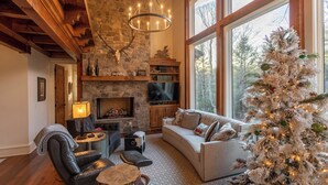 Una sala de estar acogedora con chimenea de piedra, un ventanal grande y un árbol de Navidad blanco.