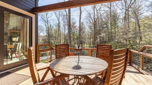 A wooden deck with a round table and chairs, overlooking a forested area. - A Robins Nest (Blowing Rock)
