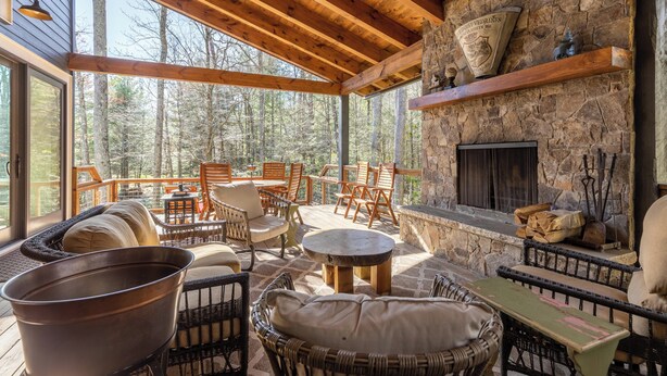 A cozy outdoor seating area with wicker furniture, a stone fireplace, and a view of the forest. - A Robins Nest (Blowing Rock)