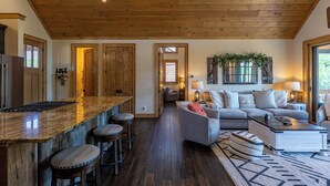 Ein großzügiger Wohnbereich mit Holzboden, eine Küche mit Bar und eine Sitzecke mit Sofa und Sesseln.