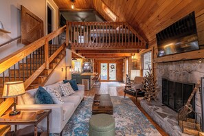 A spacious loft-style living area with a wooden staircase, a fireplace, and a kitchen in the background. - Tweetsie Den (Boone)