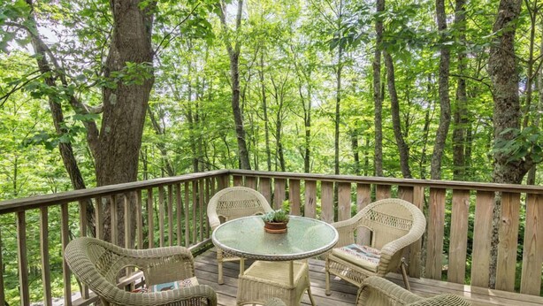A wooden deck with wicker furniture and a glass table, surrounded by a forest. - A Treetop Escape (Blowing Rock)