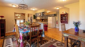 A spacious kitchen with wooden cabinets, a dining area with a table and chairs, and a chandelier. - A Treetop Escape (Blowing Rock)