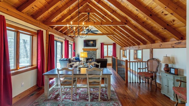 Un'accogliente sala da pranzo con pavimento in legno, un tavolo e sedie, un caminetto e vista all'esterno tramite ampie finestre.