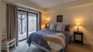 Una camera da letto con un letto grande, due lampade sui comodini, una sedia e vista panoramica tramite una porta scorrevole in vetro.