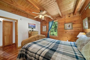 Ein Schlafzimmer einer Holzhütte mit Bett, Deckenventilator, Holzwänden und einem Fenster mit Blick.