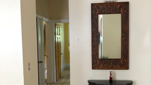 A hallway with a wooden floor, a dark wooden console table with a mirror above it, and a door leading to another room. - Cozy Mediterranean Escape  (Schenectady)