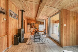 Interior em madeira com área de refeições, cozinha e uma grande porta de vidro deslizante que dá para uma varanda.
