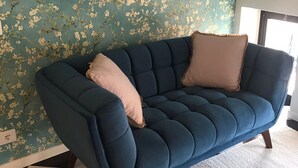 A blue sofa with a beige cushion against a floral wallpaper, a black and white checkered floor, and a white ceiling.