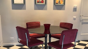 A room with a checkered floor, a round table with four red chairs, and three framed pictures on the wall.