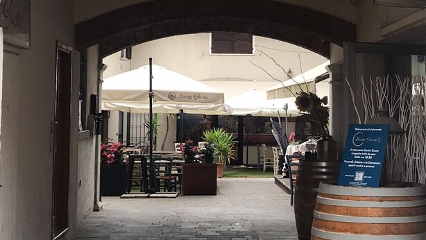 An outdoor café area with tables and umbrellas, a wooden barrel, and a signboard.