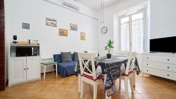 Ein Essbereich mit Tisch, Stühlen, einer Mikrowelle, einer Couch, einem Fernseher und einer Wanduhr.