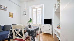 Ein Essbereich mit Tisch, Stühlen, einer Topfpflanze, einem Fernseher und einem Sofa.