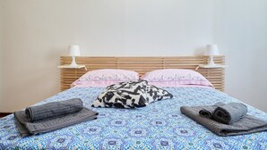 Ein Bett mit einem gemusterten Bettüberwurf, zwei Kissen, einem zusammengerollten Handtuch und zwei Nachttischlampen.
