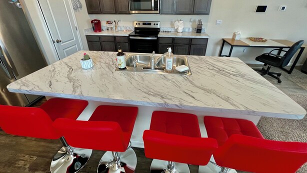 Una cocina con una isla central, taburetes rojos, un microondas y un fregadero.