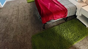 Un dormitorio con cama, ventilador de techo, ventana con persianas y alfombra verde.