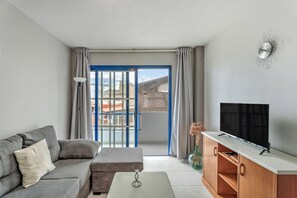 Een moderne woonkamer met een bank, een salontafel, een tv op een houten kast, en een balkon met blauwe deuren.
