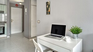 Una habitación moderna con un escritorio blanco, una computadora portátil, una planta en maceta y un cuadro en la pared.