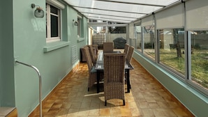 Een overdekt terras buiten met een eettafel en stoelen, een raam en een trap.