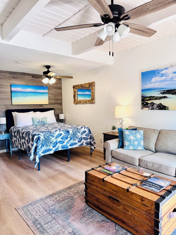 A bedroom with a bed, a sofa, a wooden chest, a ceiling fan, and wall art.