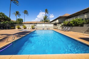 A rectangular swimming pool with a clear blue water, surrounded by lounge chairs and a fence.