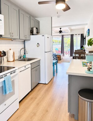 A modern kitchen with grey cabinets, a white refrigerator, and a dining area with a table and chairs. - Beach Studio, Couples Getaway! Hot Tub, Pool, AC. Video Tour. (Kihei)