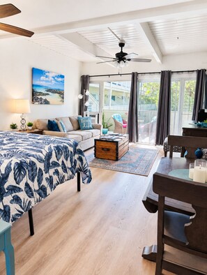 Un dormitorio con cama, escritorio, silla, ventilador de techo y vistas al exterior.