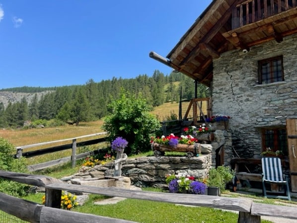 A stone building with a wooden balcony, surrounded by a wooden fence and a garden with flowers.