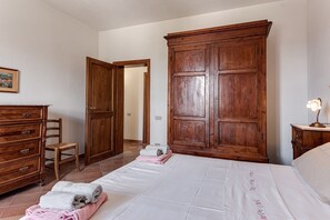 Un dormitorio con cama, un armario de madera, una silla y una mesita de noche con lámpara.