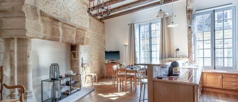 A spacious kitchen with wooden beams, a stone wall, and a large window.