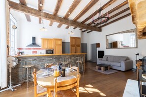 A spacious living area with a dining table set for four, a kitchen with wooden cabinets, and a gray sofa.