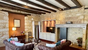 A living room with stone walls, a fireplace, two sofas, a TV, and a dining area. - La Cyprienne – Spacious House with Rooftop Terrace (Saint-Cyprien)