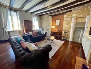 A living room with a dark-colored sofa, a wooden coffee table, and a stone wall. There is a window with blinds, a radiator, and a door leading to another room.