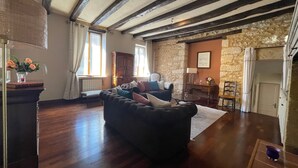 A spacious living area with a dark-colored sofa, a stone wall, and wooden beams on the ceiling. - La Cyprienne – Spacious House with Rooftop Terrace (Saint-Cyprien)
