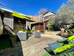 A wooden deck with outdoor furniture, a stone wall, and a wooden building with a sloped roof.