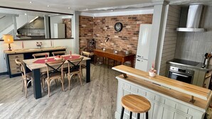 A modern kitchen with a dining area, wooden flooring, and a brick wall. - La Cyprienne – Spacious House with Rooftop Terrace (Saint-Cyprien)
