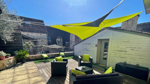 A patio with outdoor furniture, a wooden deck, and a white building with a door. - La Cyprienne – Spacious House with Rooftop Terrace (Saint-Cyprien)