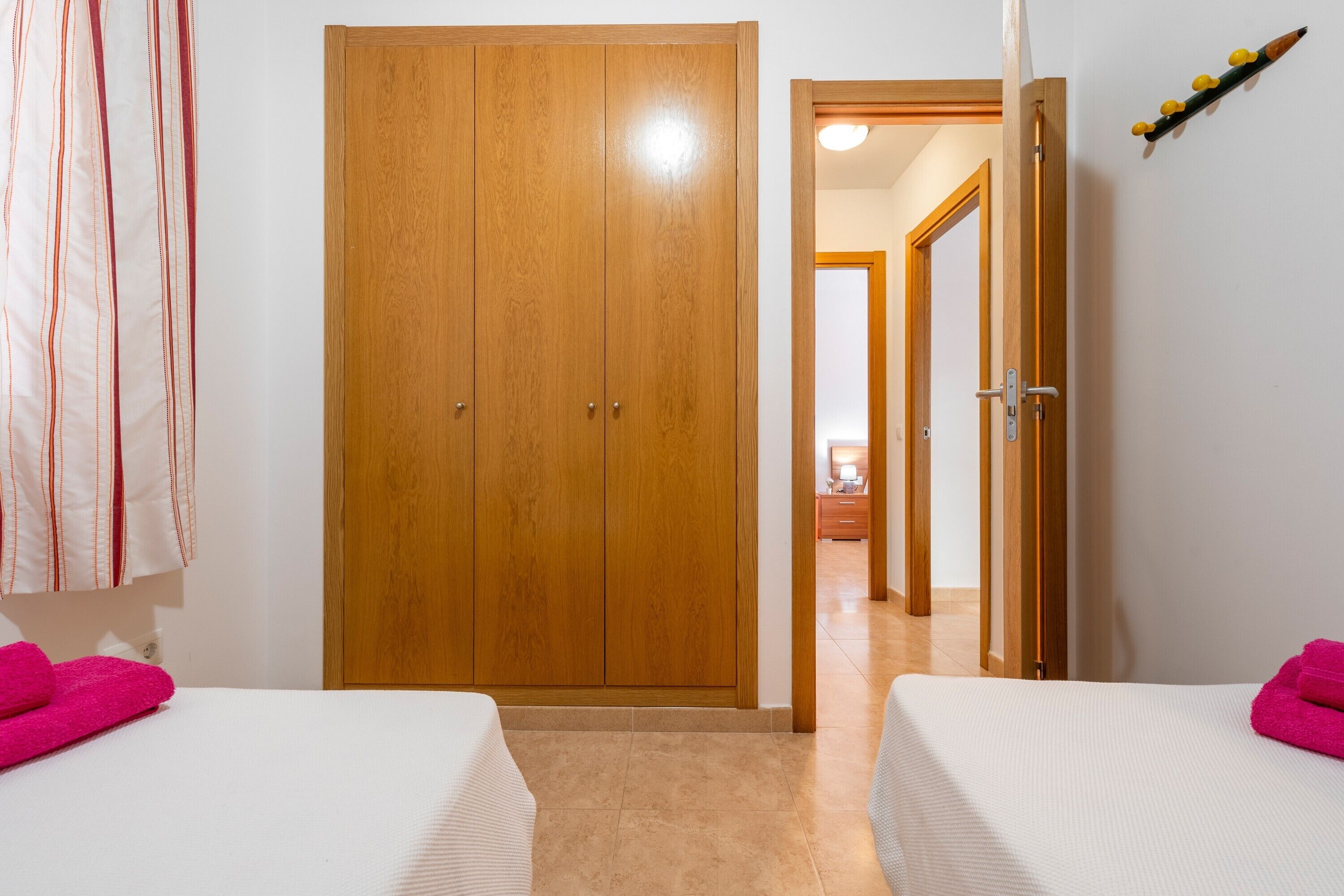 A room with two beds, a wooden wardrobe, and a bathroom visible through an open door.