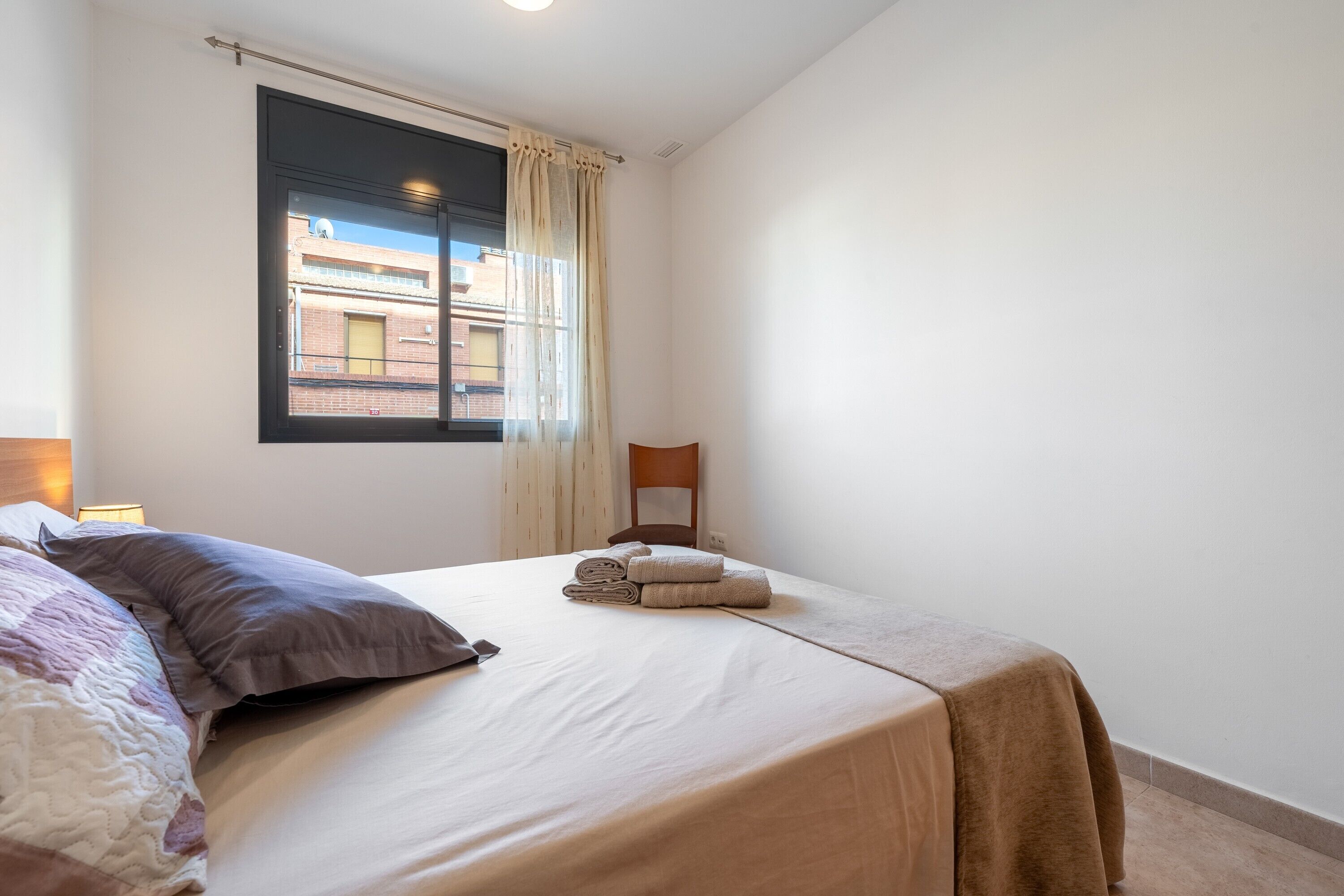 Une chambre à coucher avec un lit, une fenêtre avec des rideaux, une chaise et une lampe.