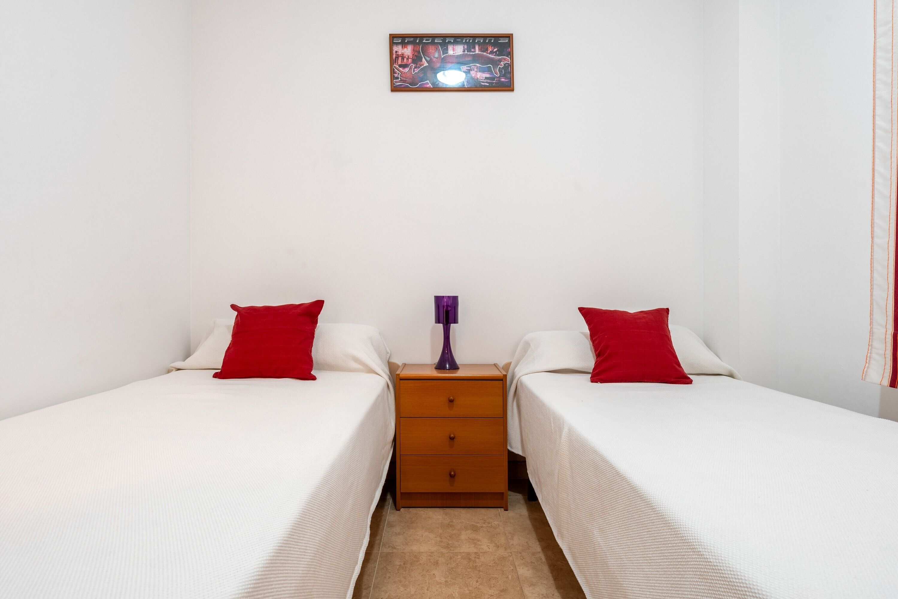 Una habitación con dos camas individuales, una mesita de noche de madera, una lámpara morada y un cuadro enmarcado en la pared.