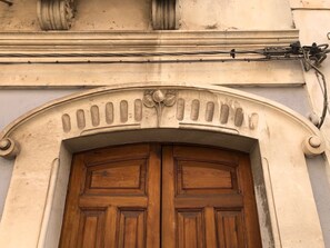 A wooden double door with a decorative arch above it, set in a building with a plain facade. - House in the Iblei Mountains (Canicattini Bagni)