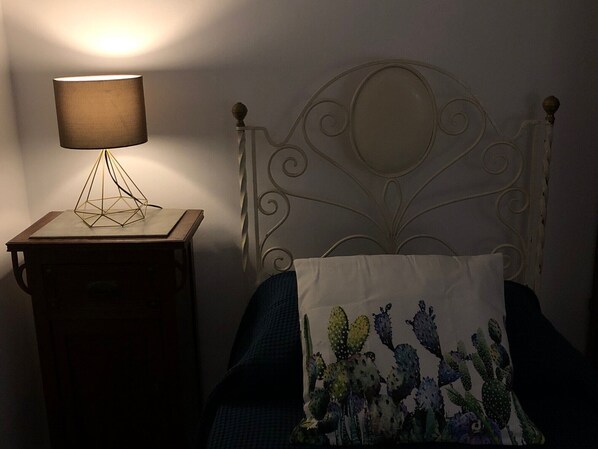A bed with a metal headboard, a nightstand with a lamp, and a cactus-themed pillow. - House in the Iblei (Canicattini Bagni)